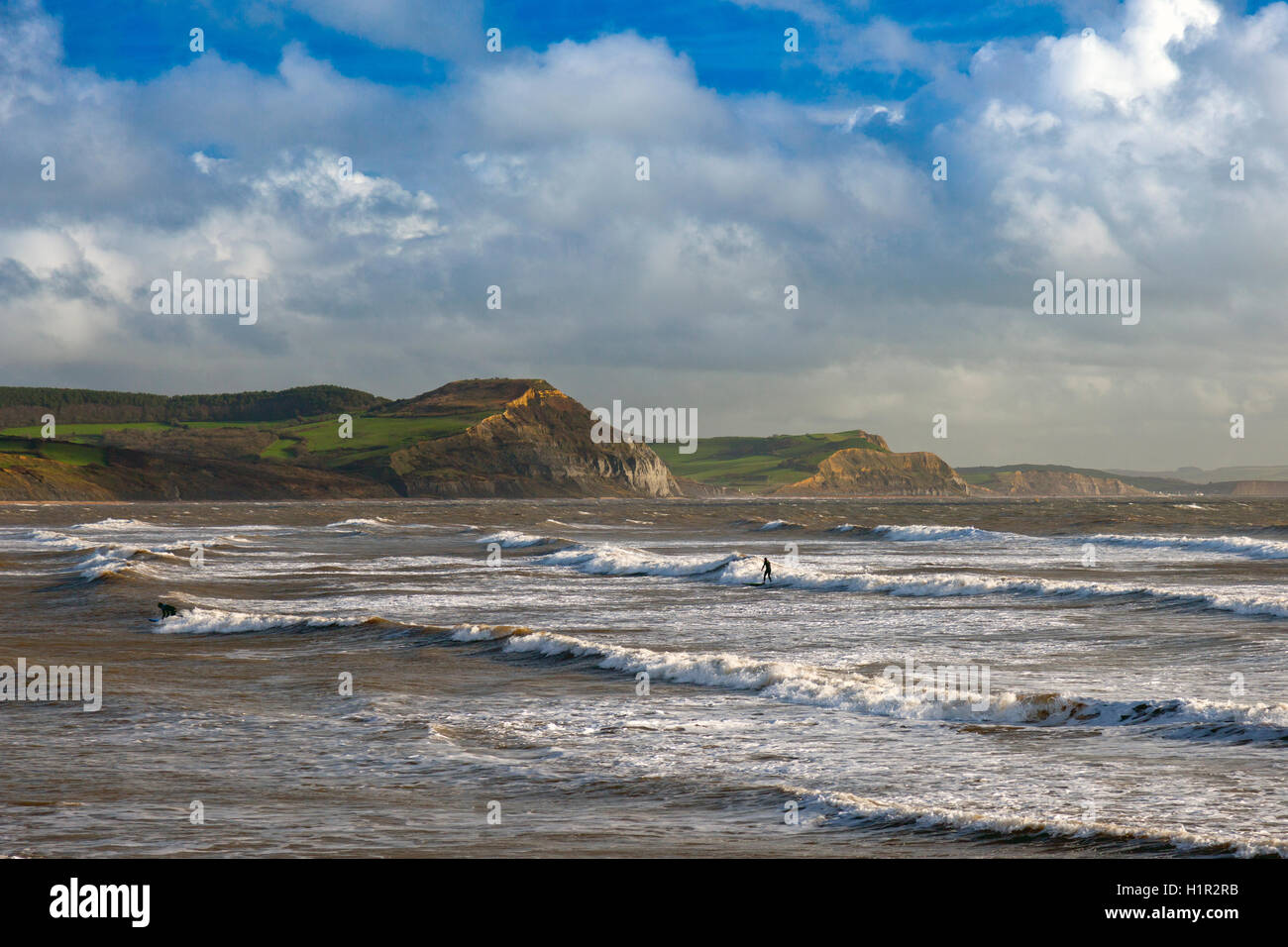 Surfer, das Beste aus den stürmischen Winterwetter bei Lyme Regis mit Golden Cap hinaus, Dorset, England, UK Stockfoto