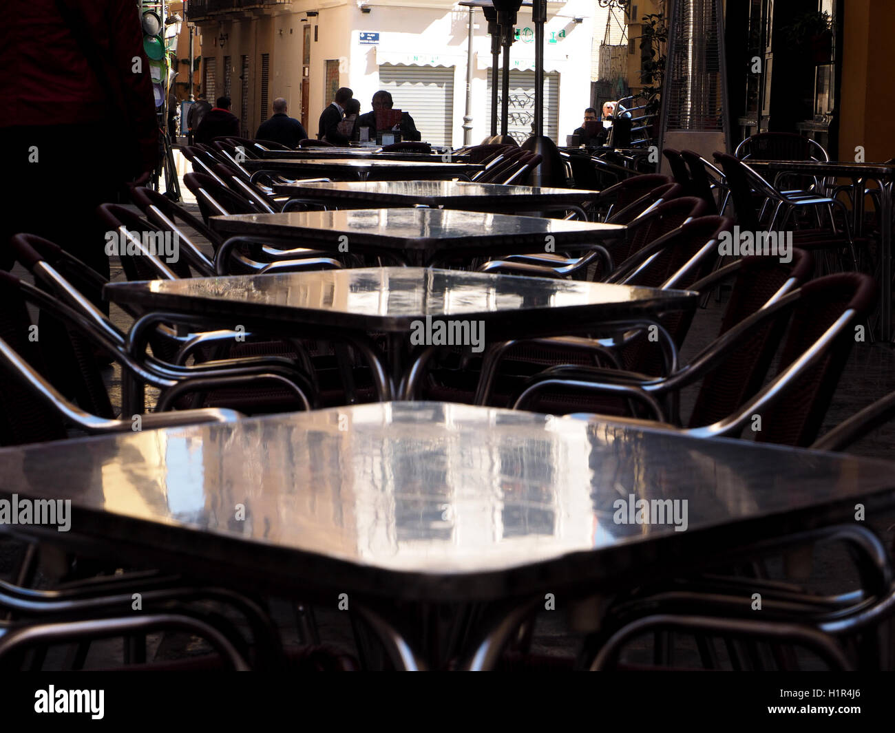 Licht fällt auf den Oberflächen der zurückweichenden Linie von schattigen Stahl Tische und Stühle in Straße Restaurant in Valencia Spanien Espana Stockfoto