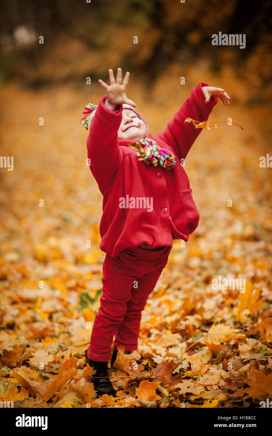Kleines Mädchen im roten Mantel im malerischen Herbst Park. Baby mit gestrickter Mütze über Laub Hintergrund. Kleinkind Kind spielt mit gelb Stockfoto