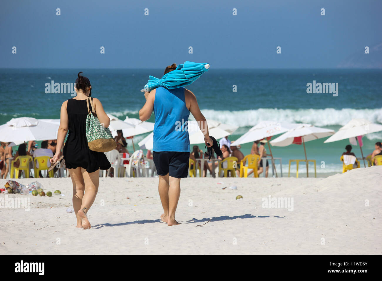 Blick auf ein paar an den Strand gehen auf sonniger Tag und klares Meerwasser. Der Mann trägt einen Regenschirm und Frau eine Strandtasche. Foto m Stockfoto