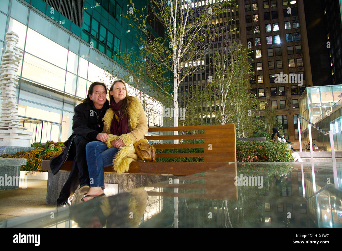 Gemischte ethnische paar sitzen auf Manhattan Bank in New York City an einem kühlen Herbst-Abend bei Bürogebäuden und Apartment-Türme Stockfoto