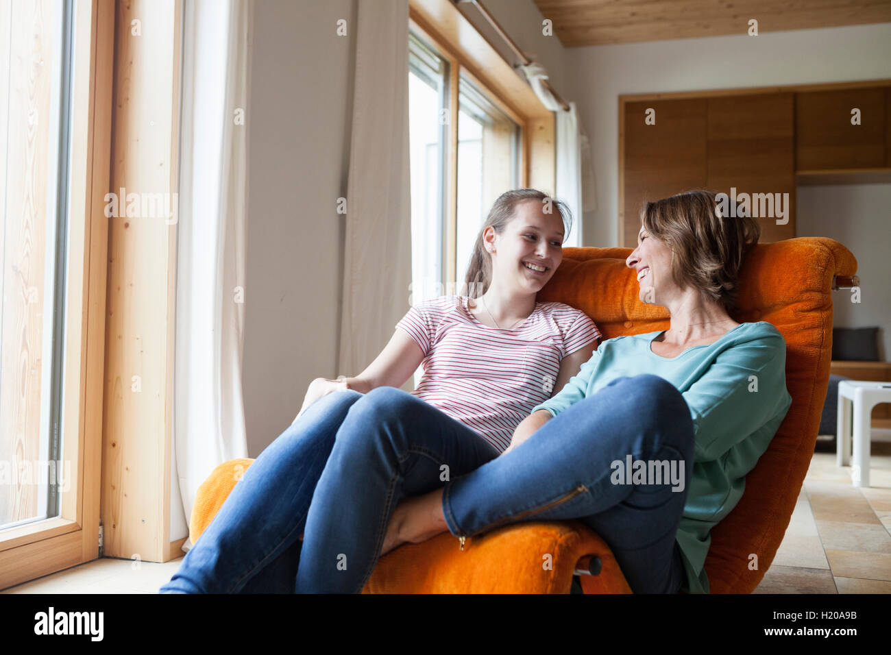Glückliche Mutter und Tochter sitzen im Sessel zu Hause Stockfoto