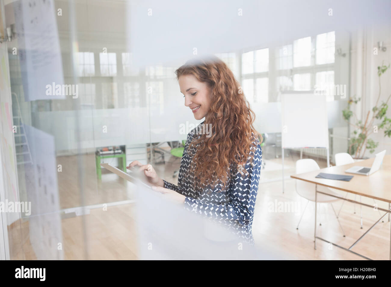 Frau im Büro mit digitalen Tablet hinter Glasscheibe Stockfoto