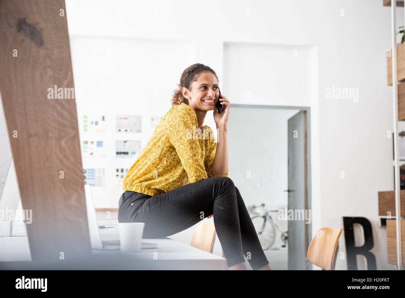 Lächelnde Frau sitzen am Schreibtisch mit Handy Stockfoto