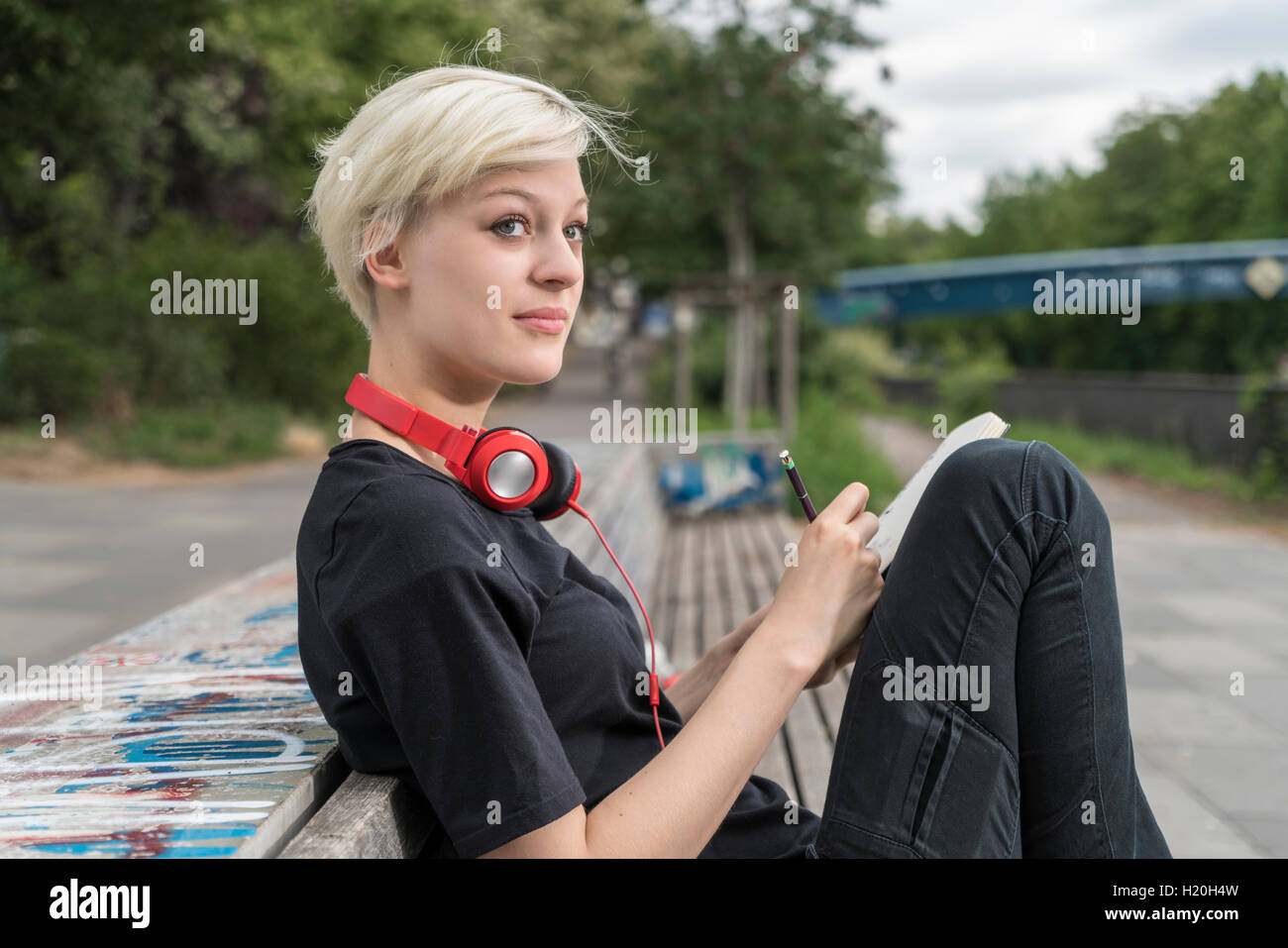 Junge Frau mit Kopfhörern auf Parkbank Stockfoto