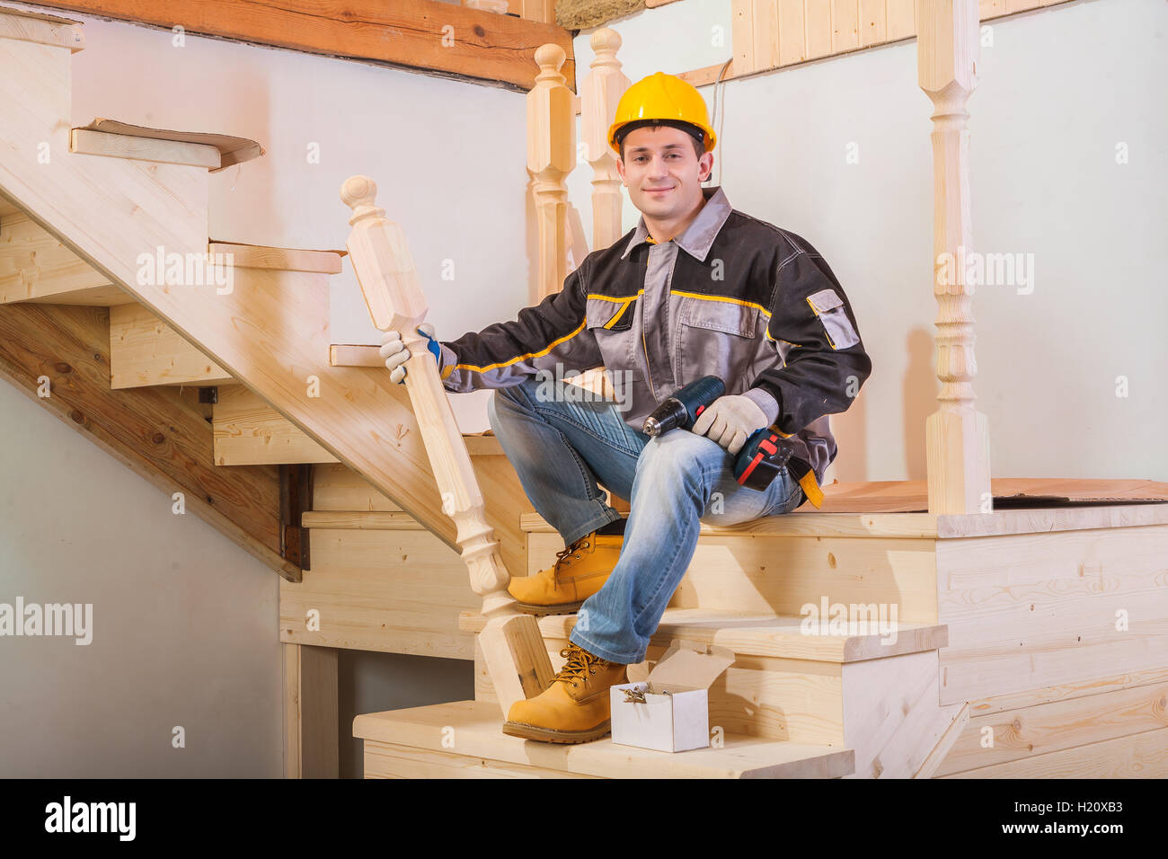 Arbeiter sitzen auf Leiter mit hölzernen Pfosten und Akku-Bohrschrauber Stockfoto