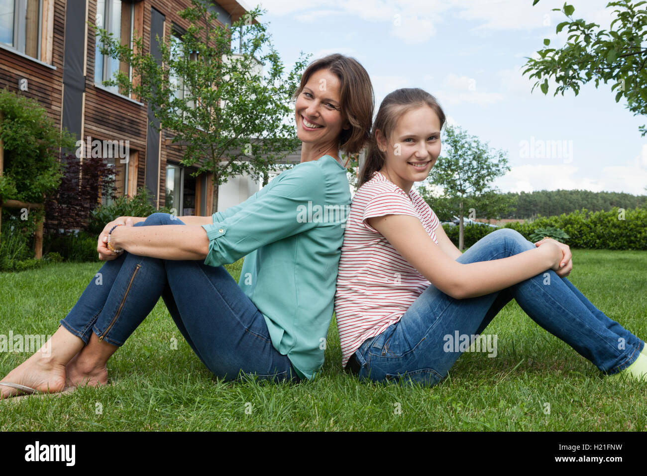 Lächelnde Mutter und Tochter sitzen Rücken an Rücken im Garten Stockfoto