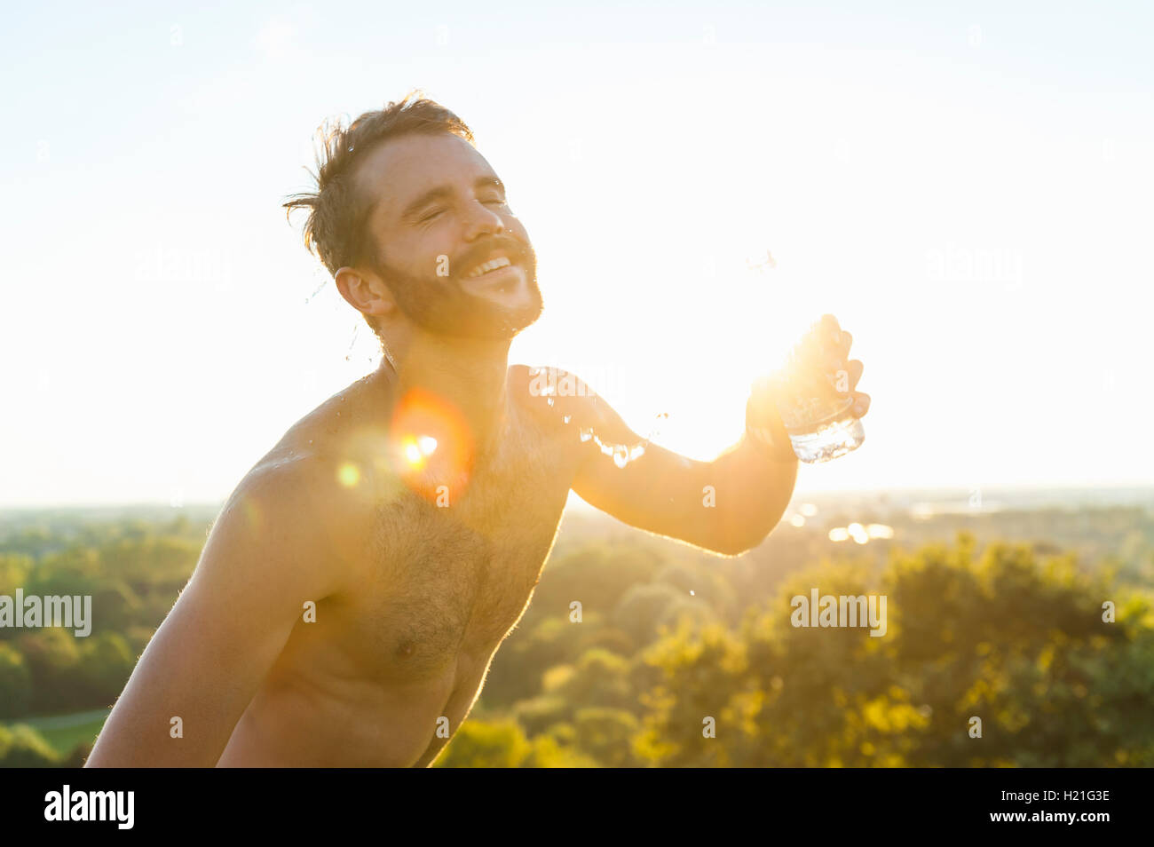Glücklich Drilliche Athlet gießt Wasser über seinen Körper bei Sonnenuntergang Stockfoto
