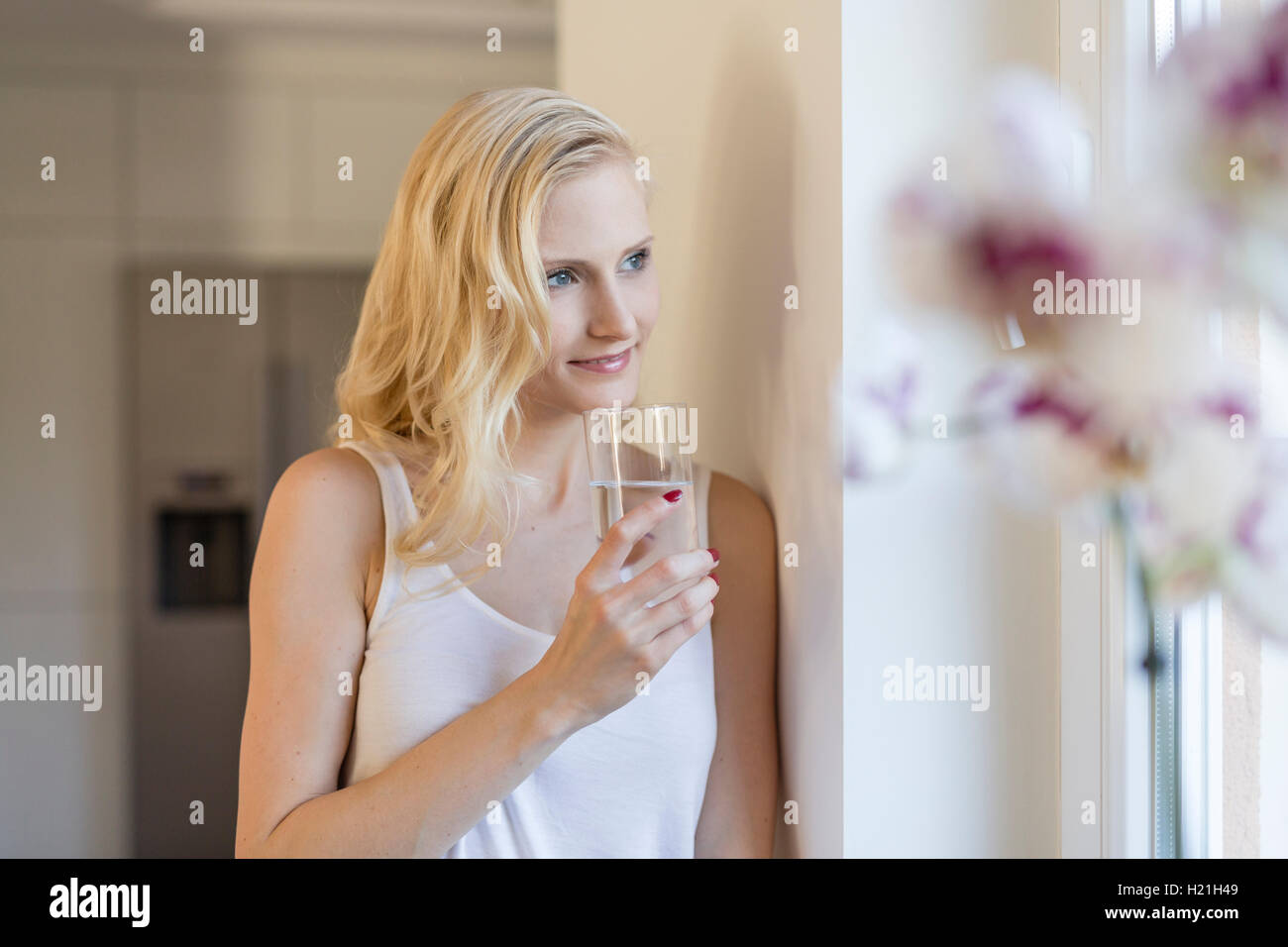 Blonde Frau mit Glas Wasser am Fenster Stockfoto