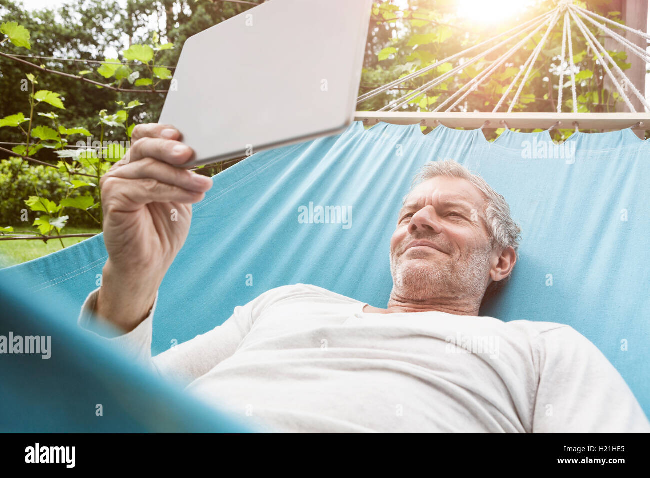 Reifer Mann mit digital-Tablette in Hängematte Stockfoto