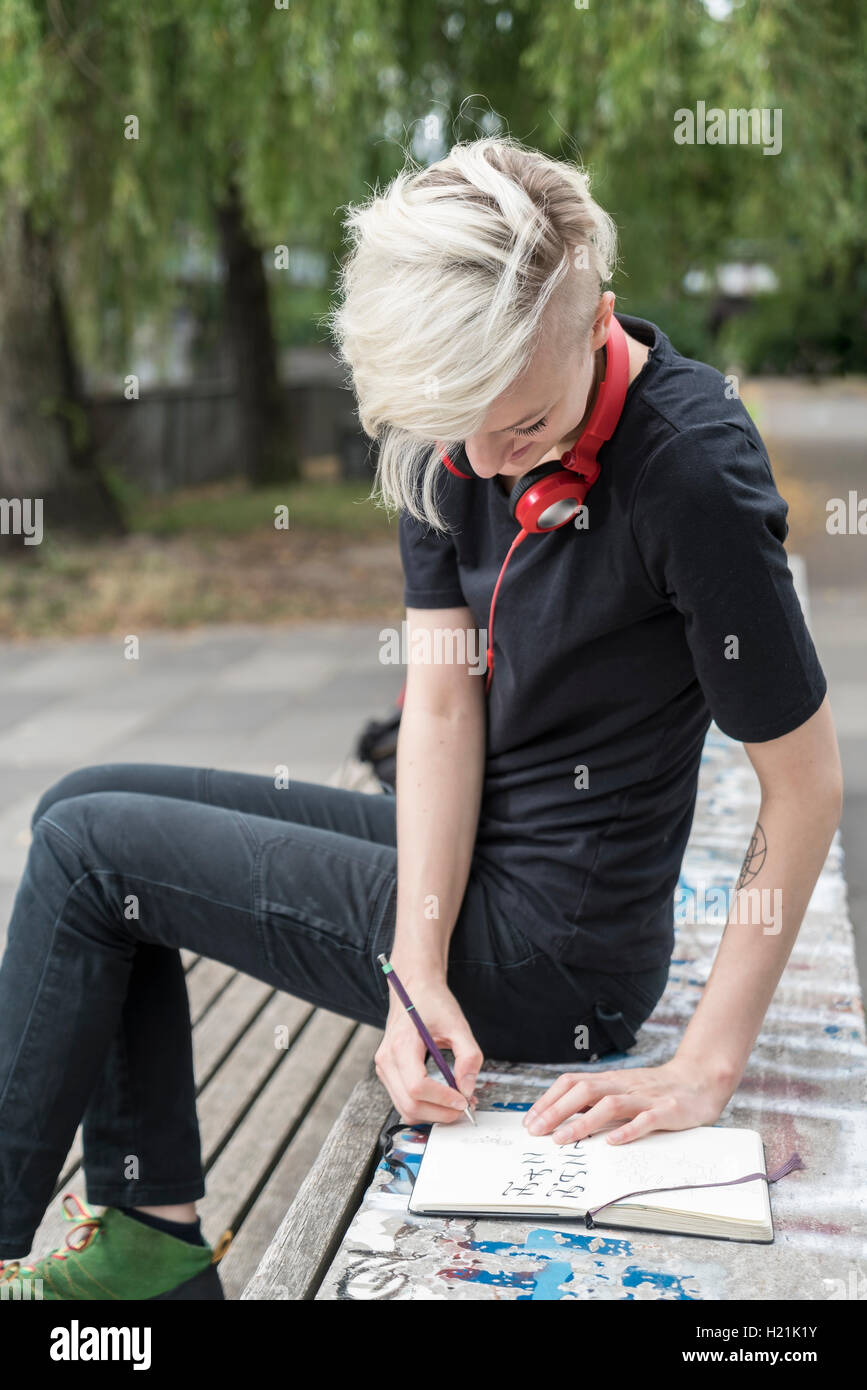Junge Frau mit Kopfhörern auf Parkbank Stockfoto