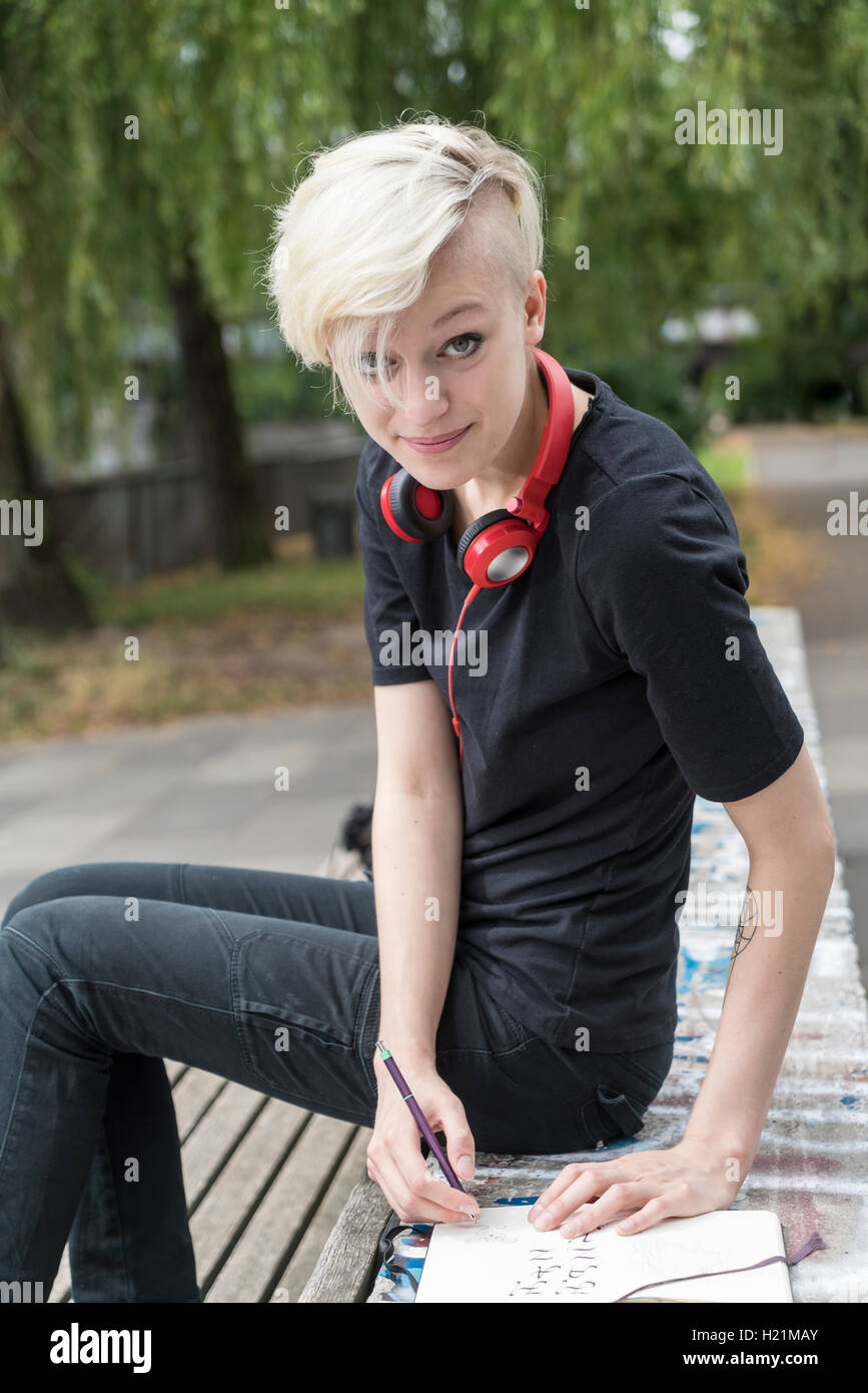 Porträt der lächelnde junge Frau mit Kopfhörern auf Parkbank Stockfoto