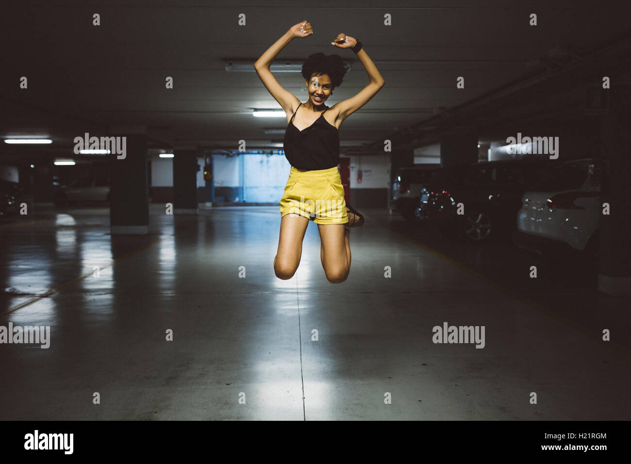 Lächelnde junge Frau springt in die Luft in einem Parkhaus Stockfoto