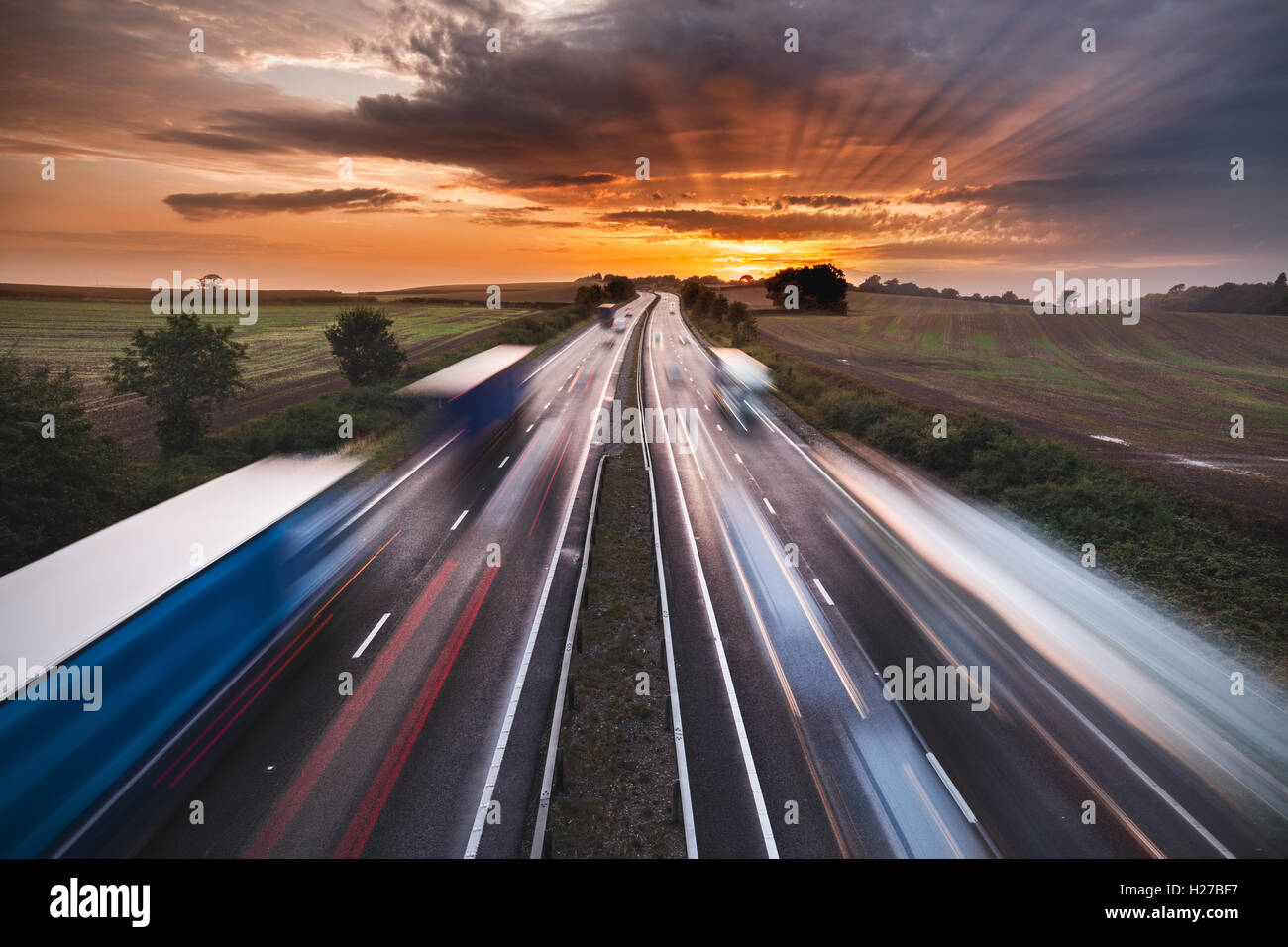 Wanderwege von Lichtern und verschwommene Formen von Fahrzeugen auf stark frequentierten Autobahn bei Sonnenuntergang Stockfoto