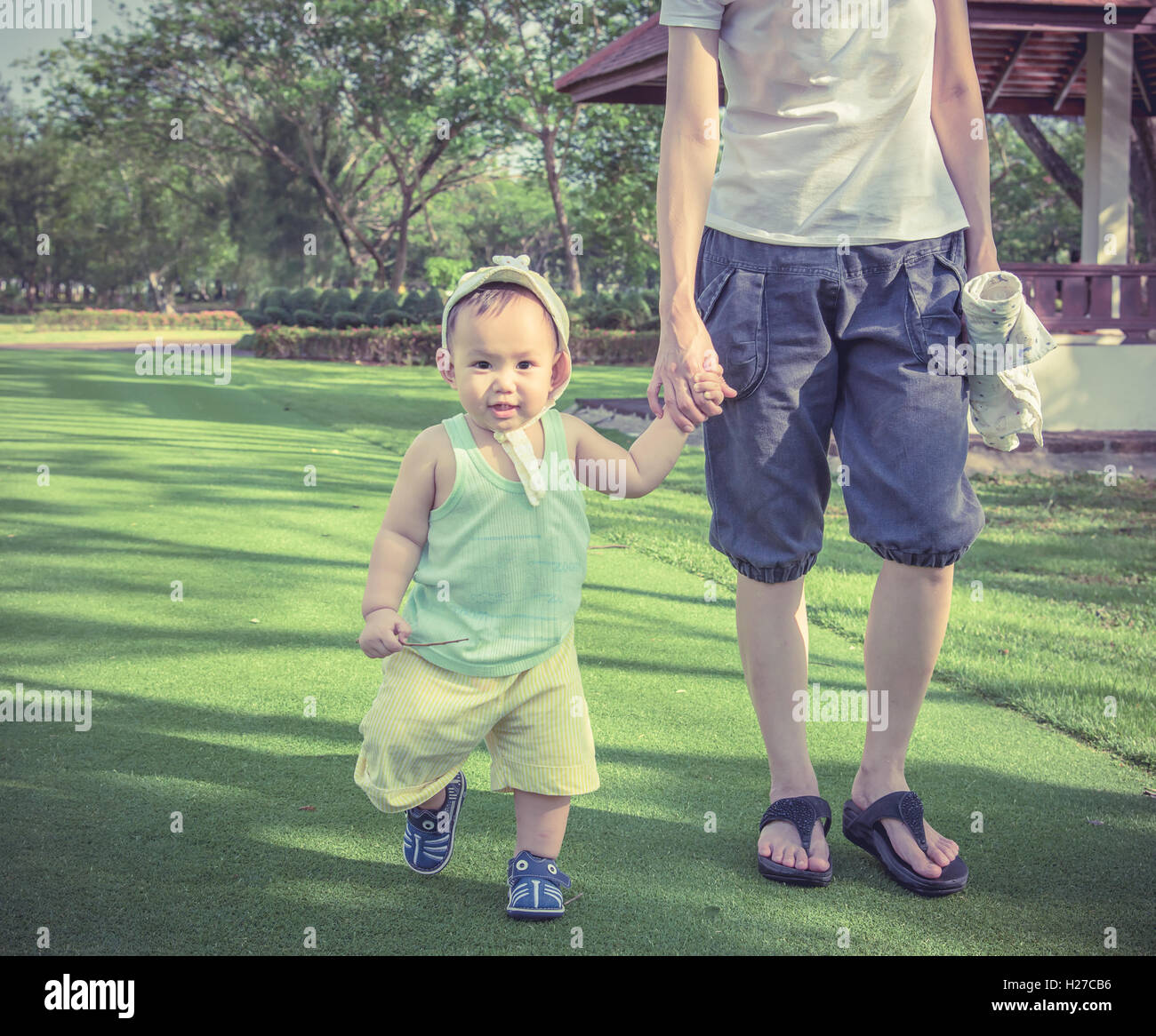 Mutter Baby Hand zu Fuß auf der Wiese im Park der Tür halten. Familie entspannende Wochenende in Thailand Stockfoto