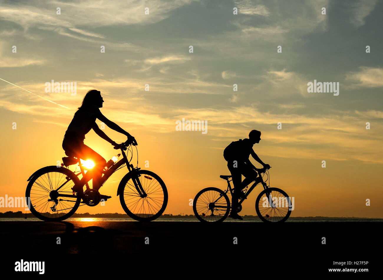 Personen mit Fahrrad auf der Mole bei Sonnenuntergang Stockfoto