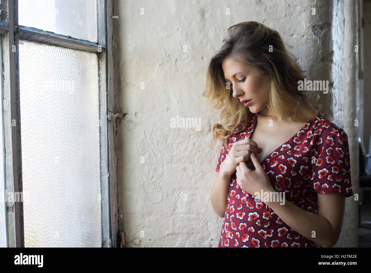 Schöne junge Frau im roten Kleid am Fenster übergibt Herz Stockfoto