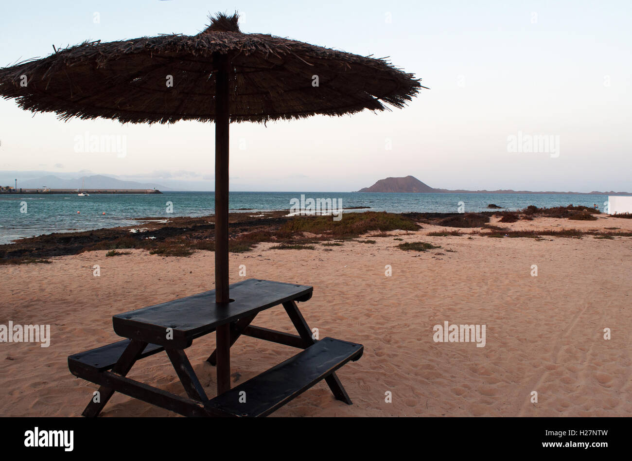 Fuerteventura, Kanarische Inseln, Nordafrika, Spanien: Tisch und Sonnenschirm am Strand mit Blick auf die Caldera, den Vulkan der Insel f Lobos Stockfoto