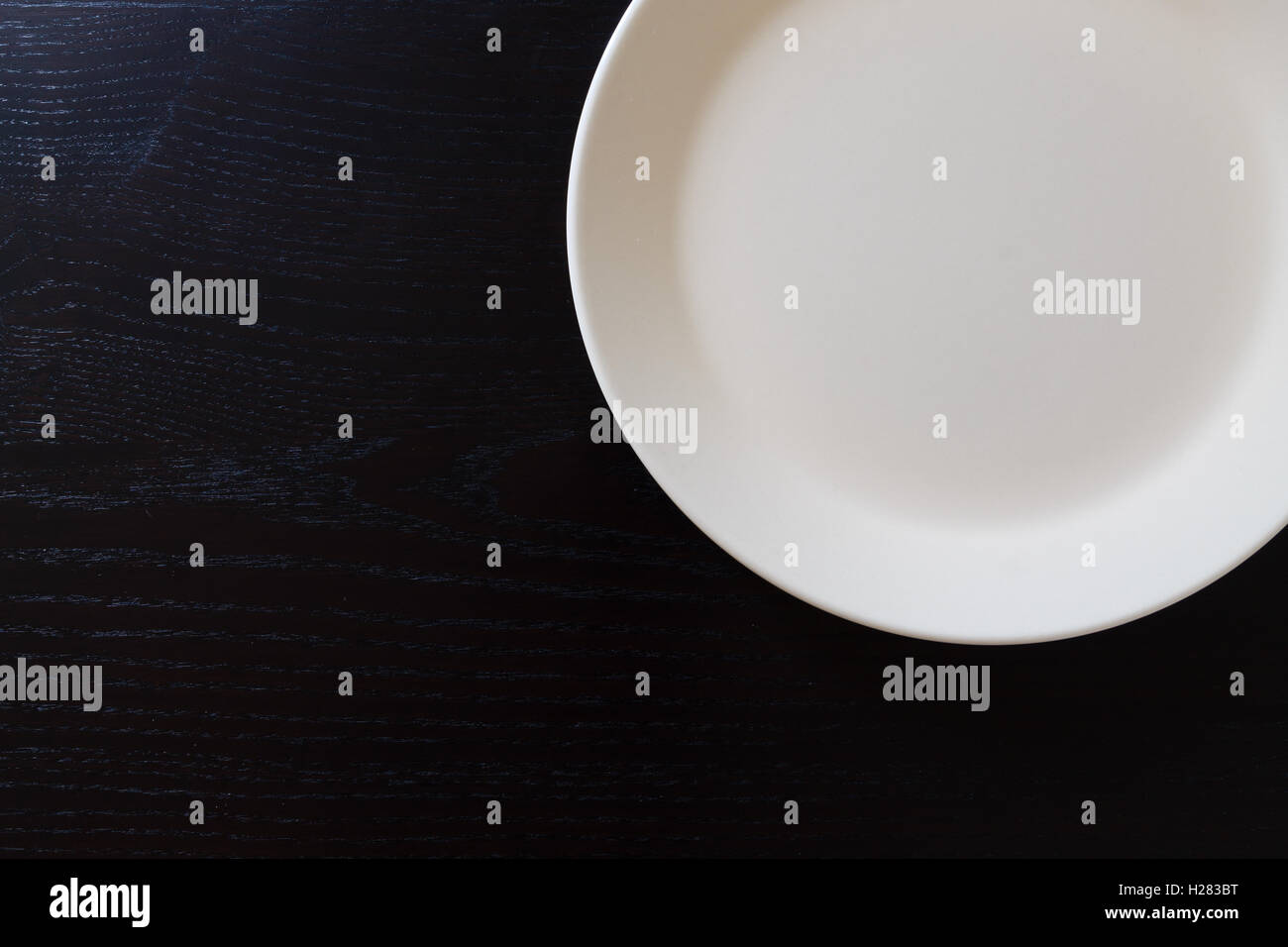 Leere weiße Platte auf schwarzer Holztisch. Küchenhelfer hautnah Stockfoto