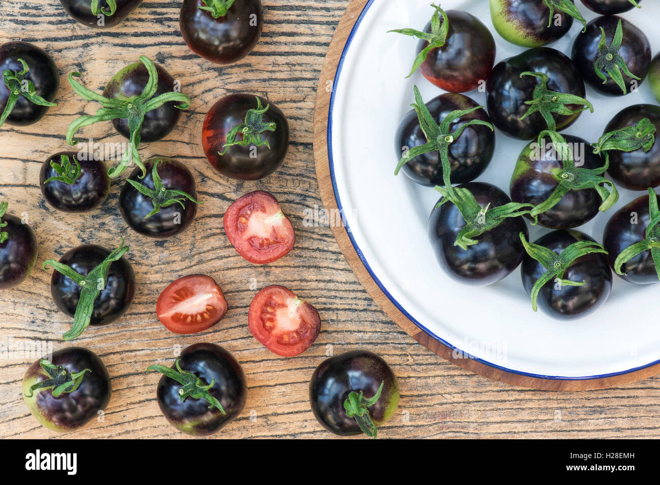 Schwarze Tomaten Indigo Rose ganze und halbierte auf ein Emaille-Schild Stockfoto