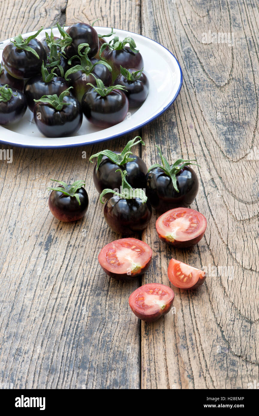 Schwarze Tomaten Indigo Rose ganze und halbierte auf ein Emaille-Schild Stockfoto