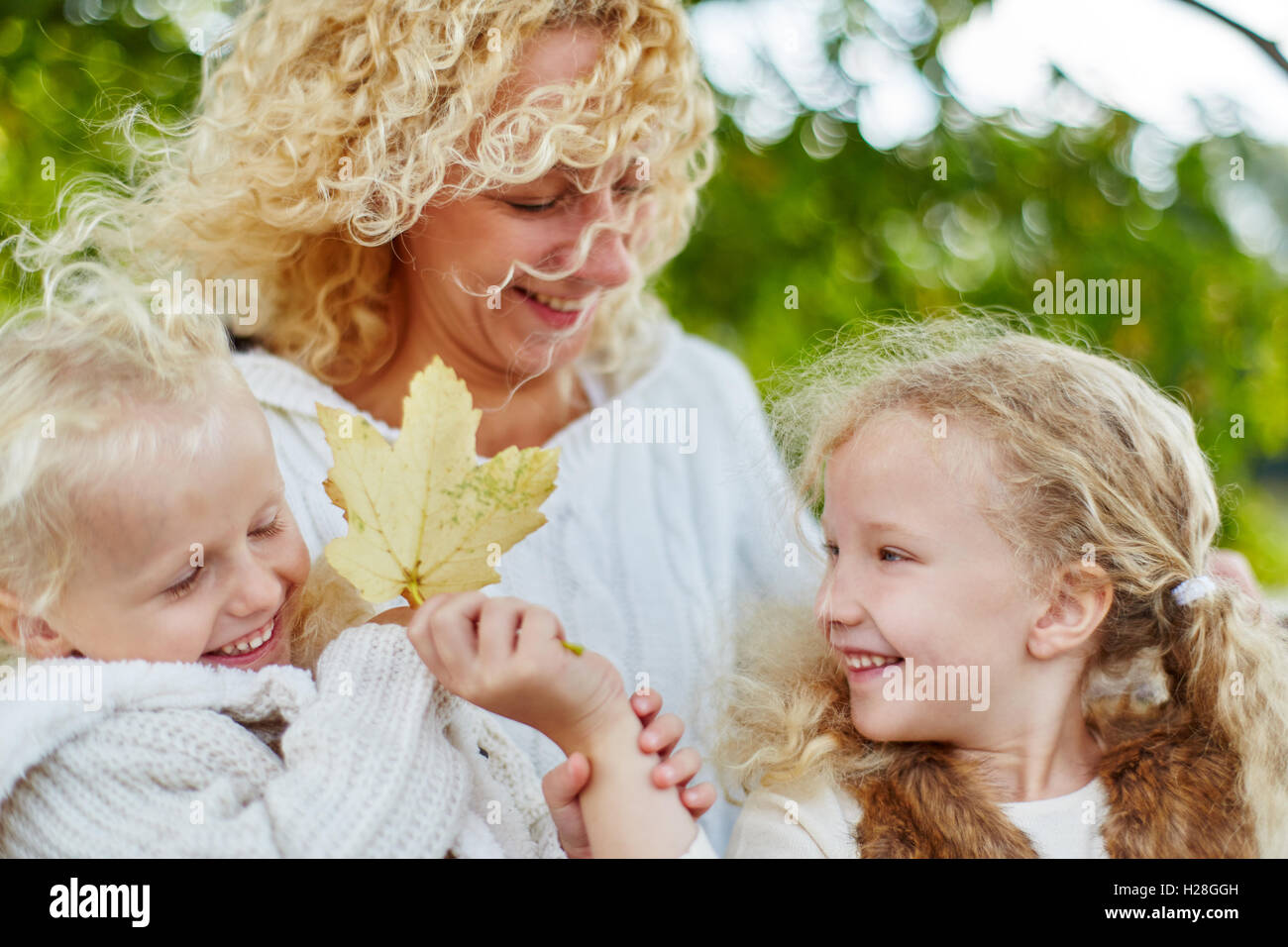 Schwestern und Mutter mit Herbstlaub in der Natur spielen Stockfoto