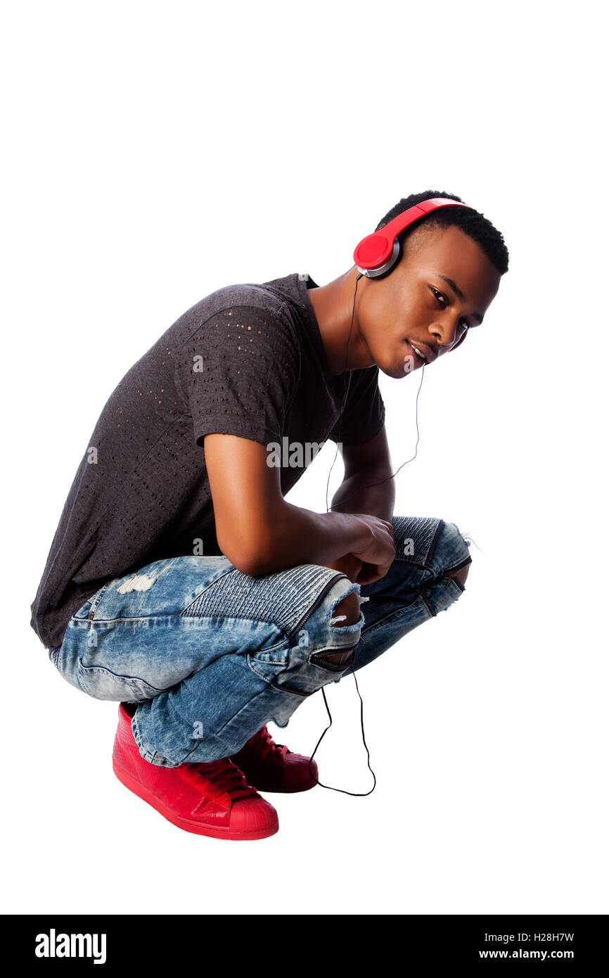 Schöne afrikanische Teenager Musikhören tragen rote Kopfhörer beim hocken, auf weiß. Stockfoto