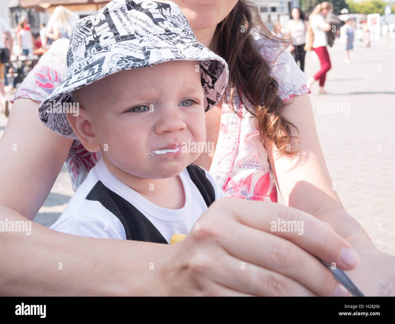 Schöne Kleinkind zu Fuß mit seiner Mutter auf eine Städtereise. Junge essen Suppe Sauerrahm der Straße. Kid stilvoll gekleidet Schmetterling und Kappe Stockfoto