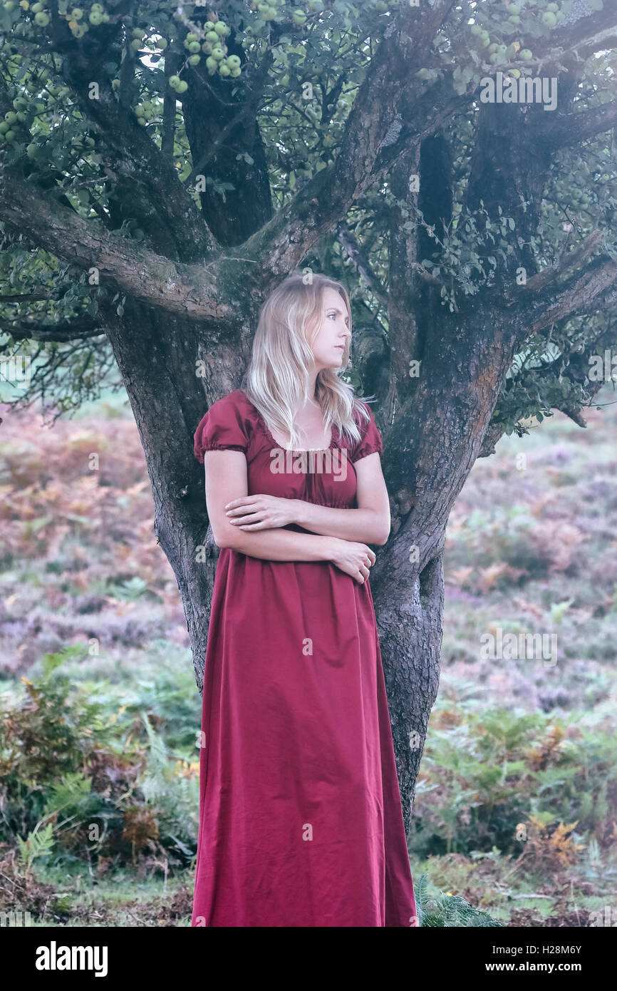 eine blonde Frau mit einem roten Kleid steht unter einem Baum Stockfoto