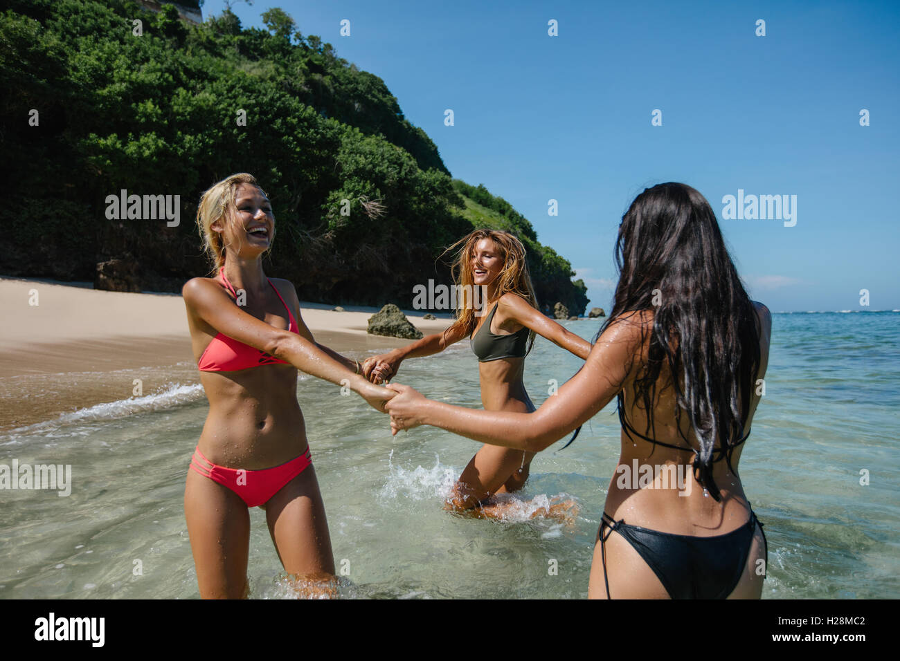 Schuss von drei jungen Frauen spielen mit Hand in Hand am Strand. Frauen im Bikini spielen Ring um die rosigen im Meer Wasser. Stockfoto