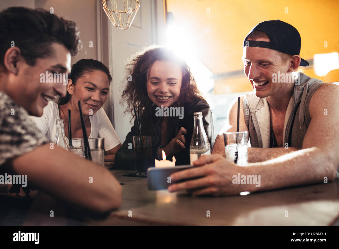 Fröhliche junge Freunde Smartphone betrachten, während Sie im Café sitzen. Gemischte Rassen Menschen sitzen an einem Tisch im Restaurant mit mo Stockfoto