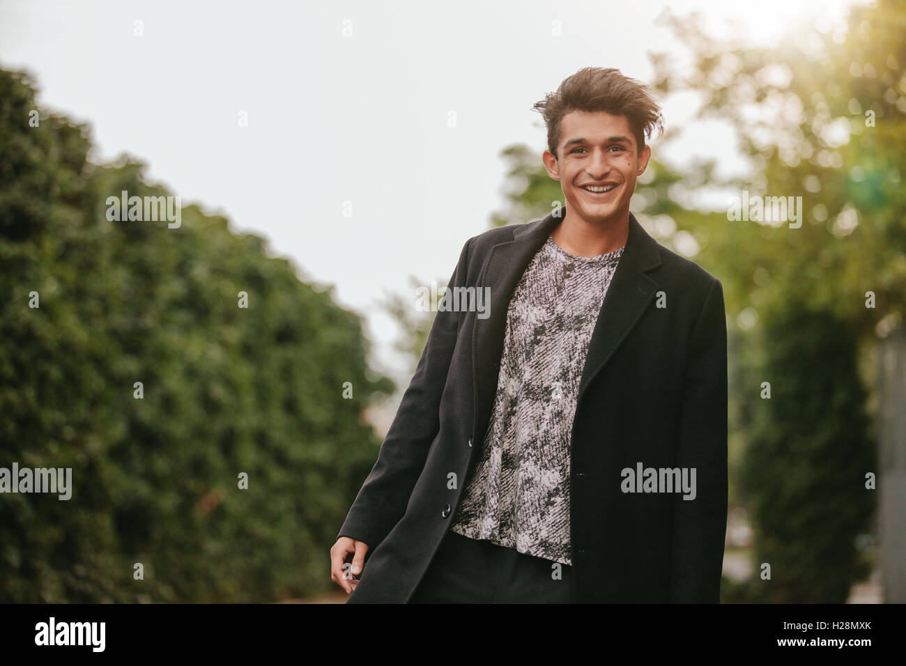 Porträt von gut aussehenden jungen Mann stehend im freien Blick in die Kamera und lächelnd. Teenager Kerl in Casuals suchen glücklich. Stockfoto