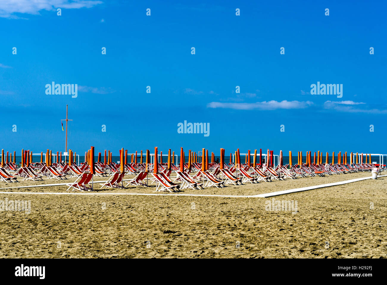 Leere orange Liegestühle und Sonnenschirme am Strand, am Anfang der Saison, Viareggio, Toskana, Italien Stockfoto