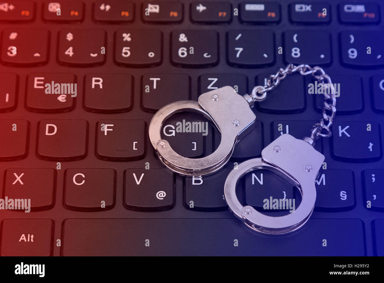 Cybercrime-Konzept mit kleinen Handschellen auf Computer-Tastatur Stockfoto