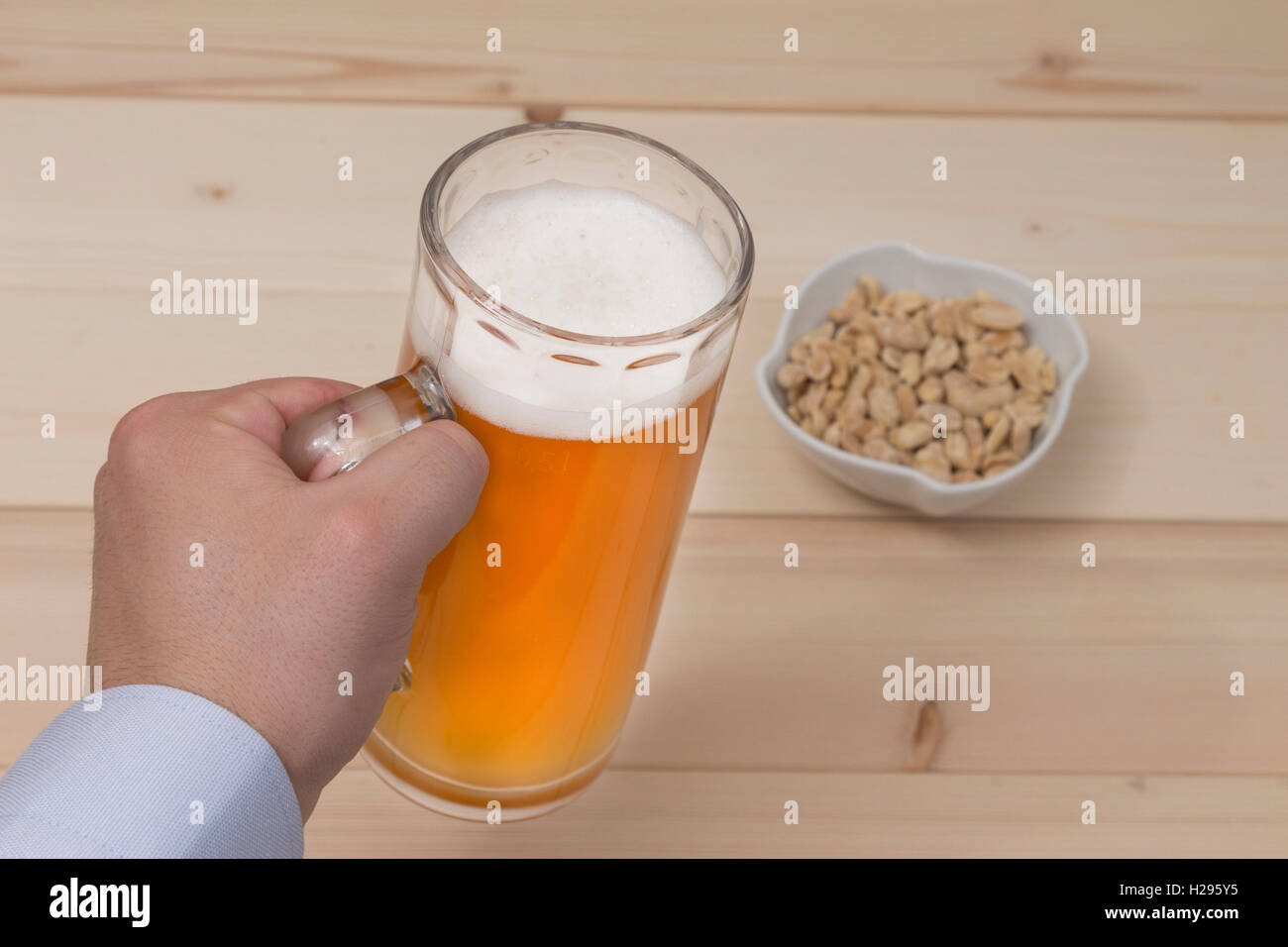 Männliche Hand hält einen Becher Bier vom Fass. Erdnüsse in der Schale auf den Tisch. Stockfoto