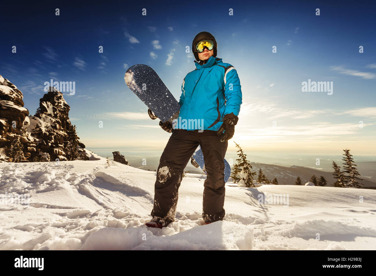 Snowboarder posiert auf blauen Himmel Hintergrund in Bergen Stockfoto