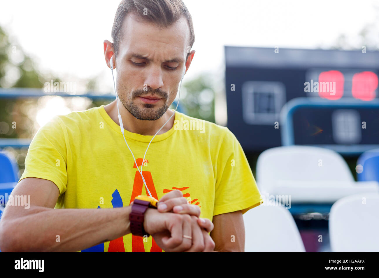 Sportlicher Mann, Blick auf die Uhr beim hören von Musik im Stadion Stockfoto