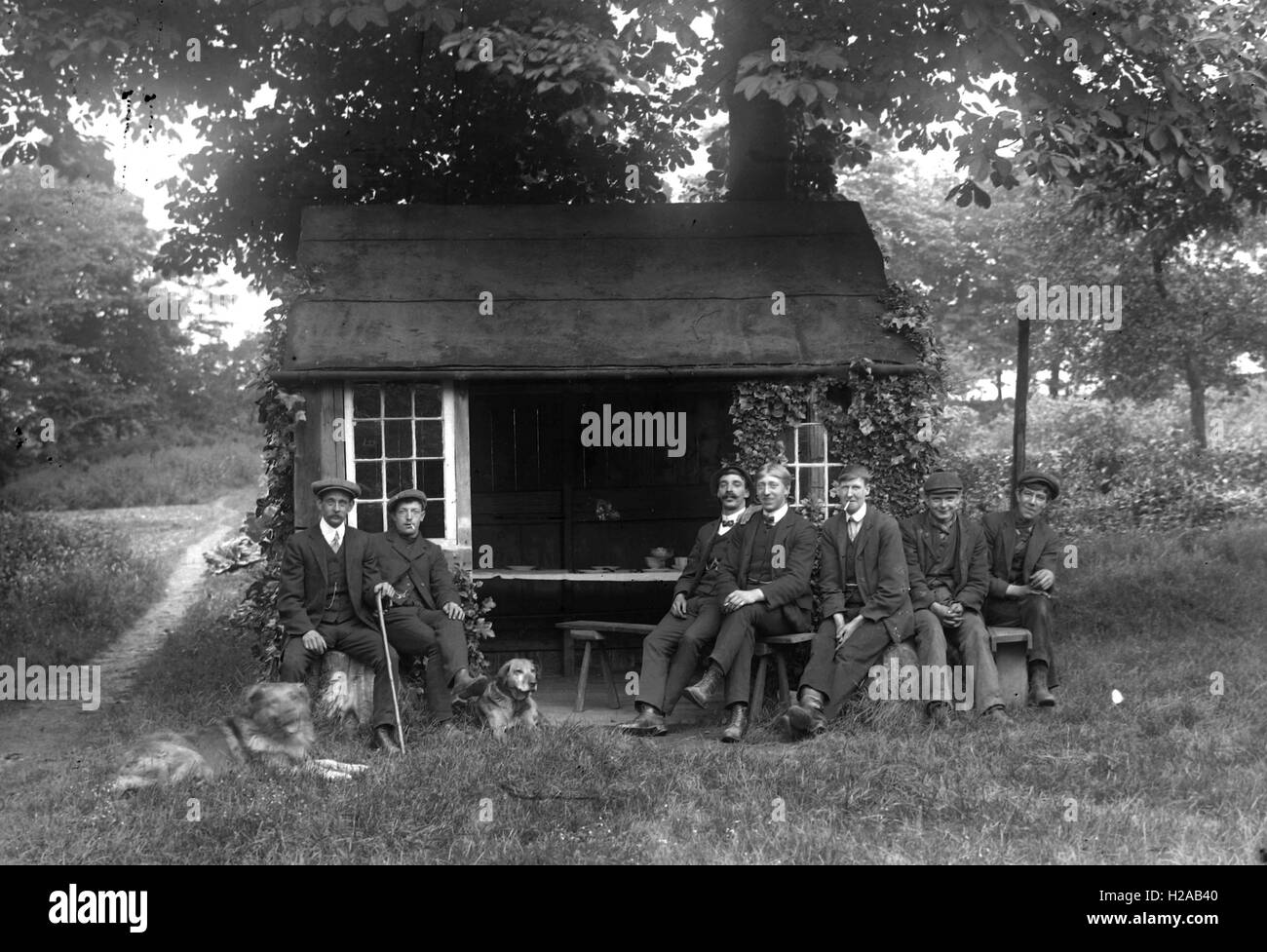 Männer mit Hunden posiert auf was ein ländliches Refugium oder Jagdhütte sein kann. 1900. Foto von Tony Henshaw Stockfoto