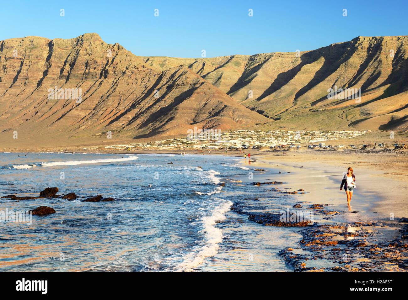 Junge Frau zu Fuß am Strand Playa La Caleta de Famara mit Klippen von Risco de Famara. Lanzarote, Kanarische Inseln Stockfoto