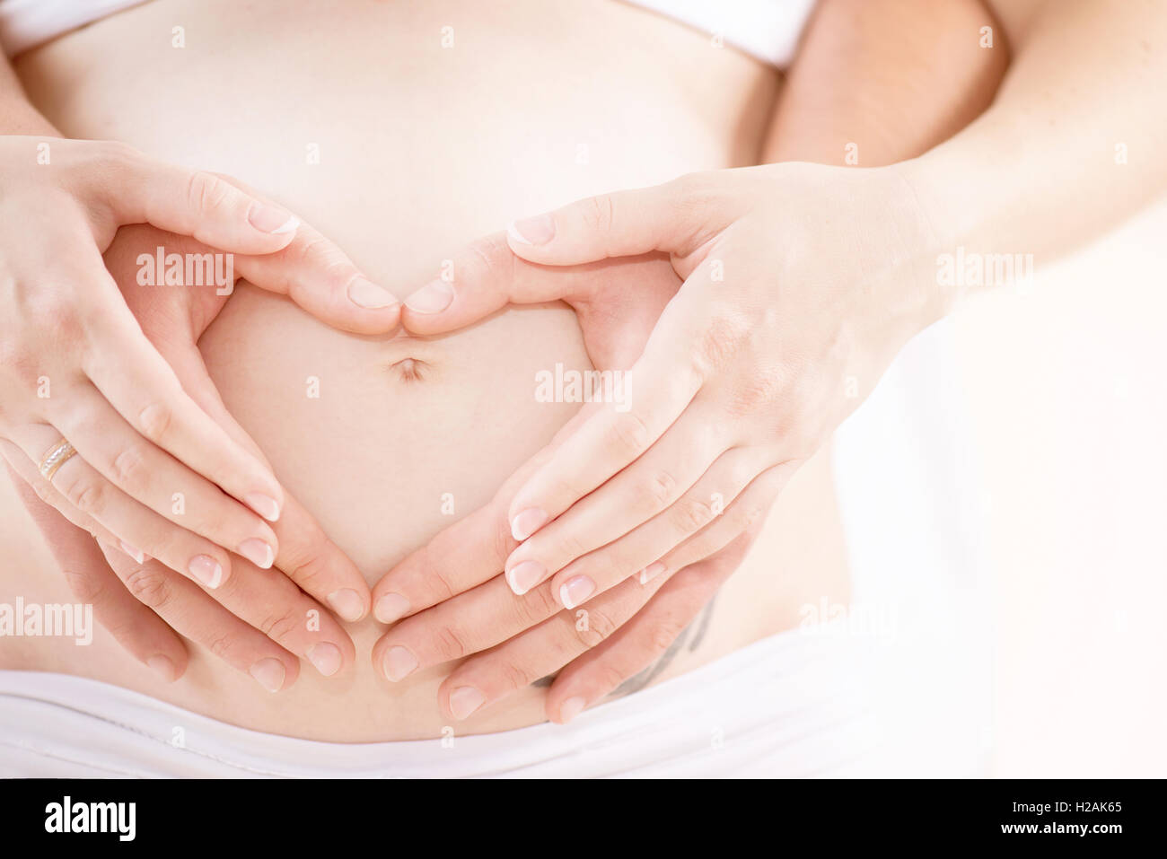 Paar erwartet Baby. Schwangeren Bauch mit Fingern Herzsymbol Stockfoto
