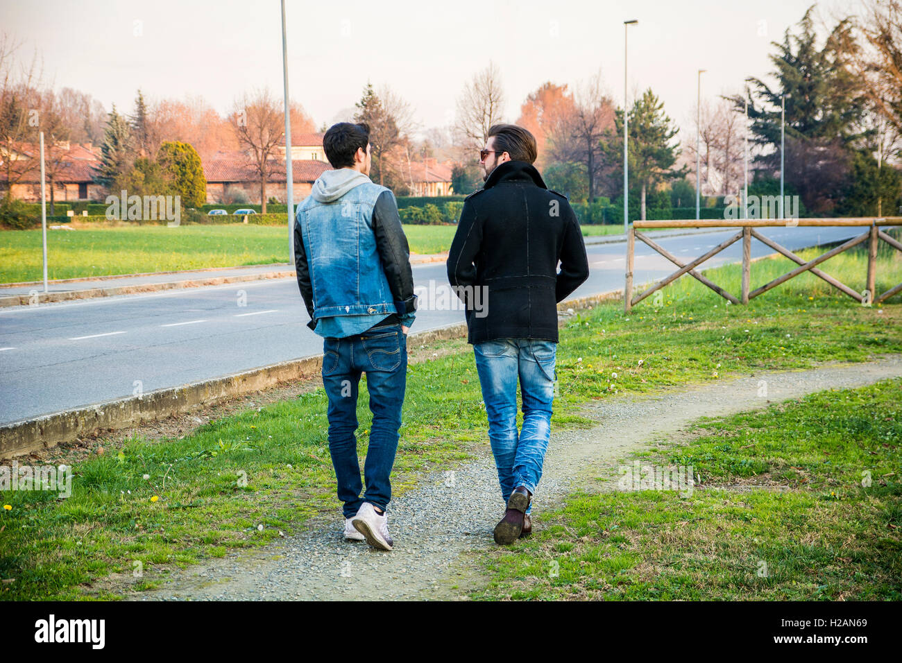 Zwei schöne lässig trendige junge Männer, 2 Freunde in einem städtischen Park zu Fuß und im Chat zusammen Stockfoto