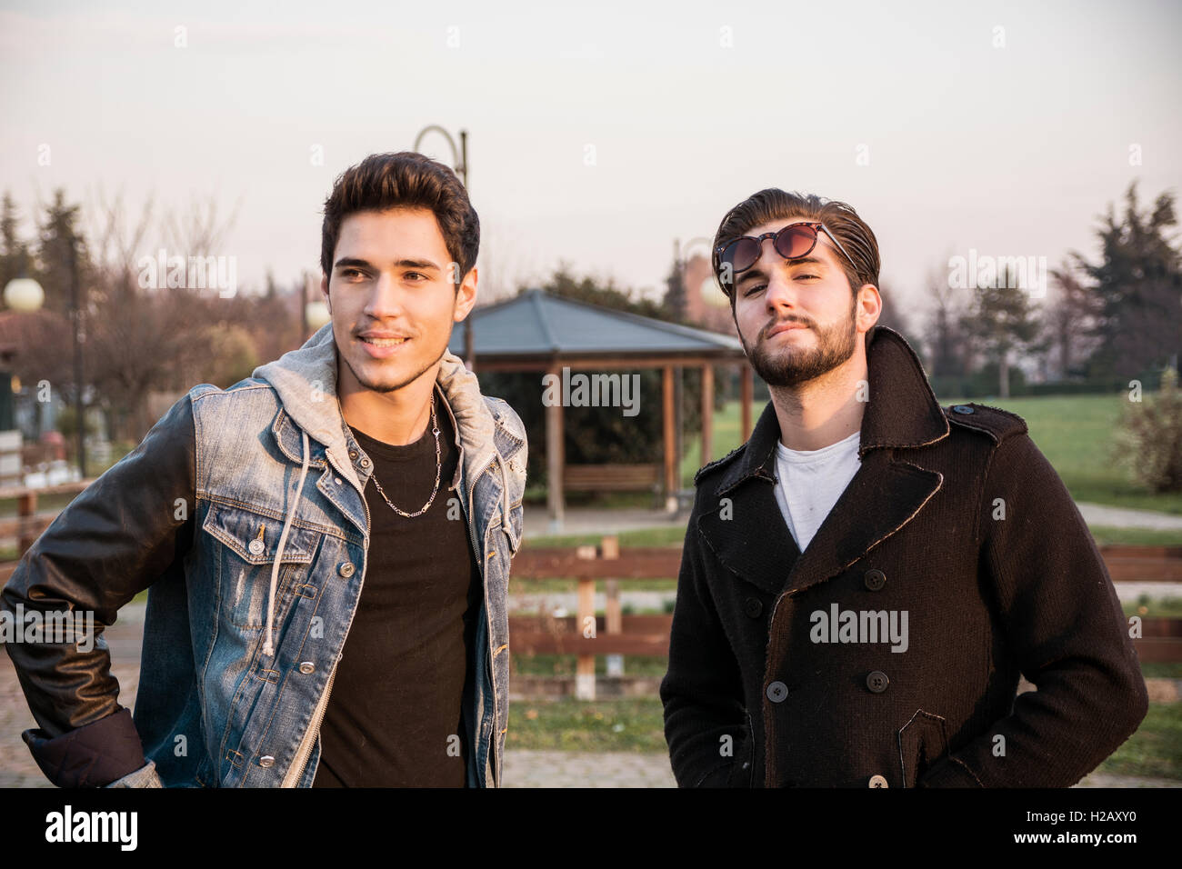 Zwei schöne lässig trendige junge Männer, 2 Freunde in einem städtischen Park zu Fuß und im Chat zusammen Stockfoto
