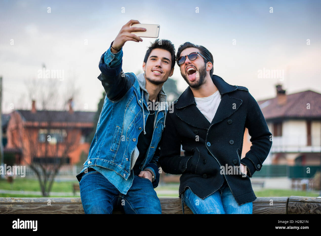 Zwei junge Männer, die die Selfie sitzend auf Bank im freien Stockfoto