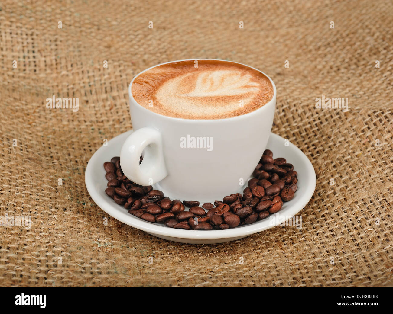 Cappuccino mit Kaffeebohnen auf Jute-Hintergrund Stockfoto