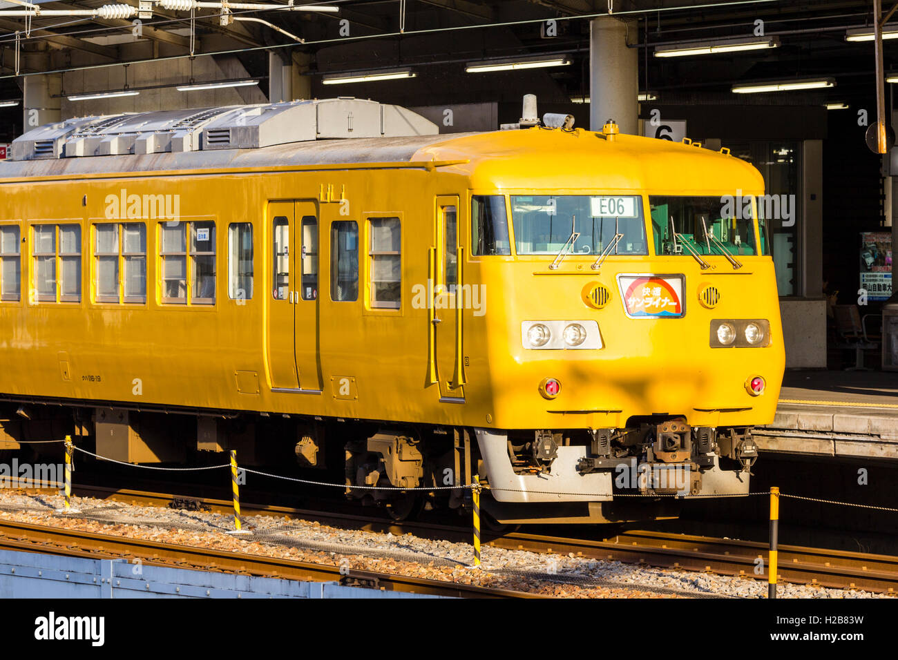 Japan. Fukuyama. Japanische Bahnhof, der vordere Teil der gelb E117 elektrische Eisenbahn, Auto, S-Bahn an der Plattform. Starker Sonneneinstrahlung. Stockfoto