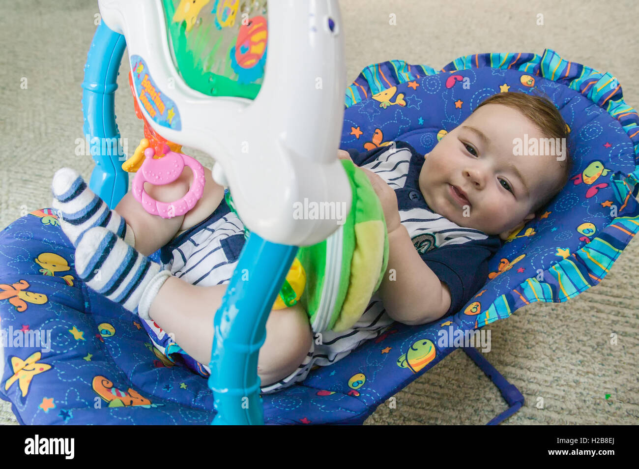 Vier Monate altes Baby junge liegend in einem Schaukelstuhl sitzen in seinem Haus, unterhalten sich mit dem obenliegenden Spielzeug Stockfoto