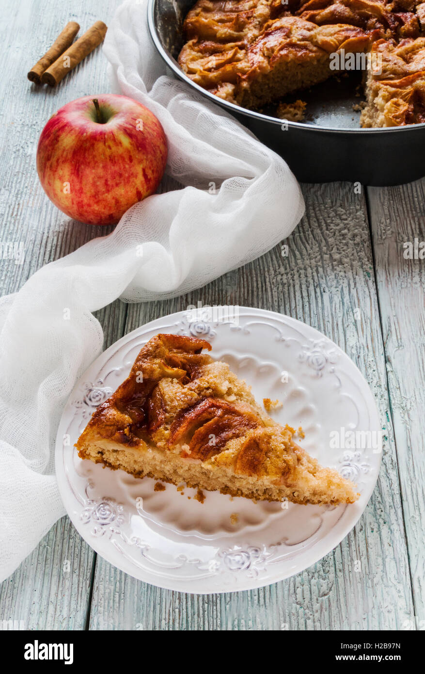 Stück hausgemachten süßen Apfel und Zimt Kuchen auf Vintage weißen Teller. Pie in eine Auflaufform und frisches Obst auf hölzernen Hintergrund. Stockfoto