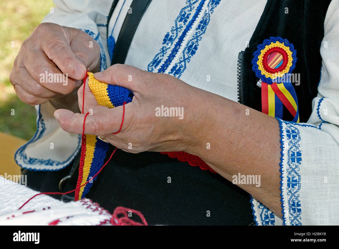 Alte Frau, gekleidet in rumänischen Trachten, verwebt mit der hand ein Gürtel in Nationalfarben und Design. Stockfoto