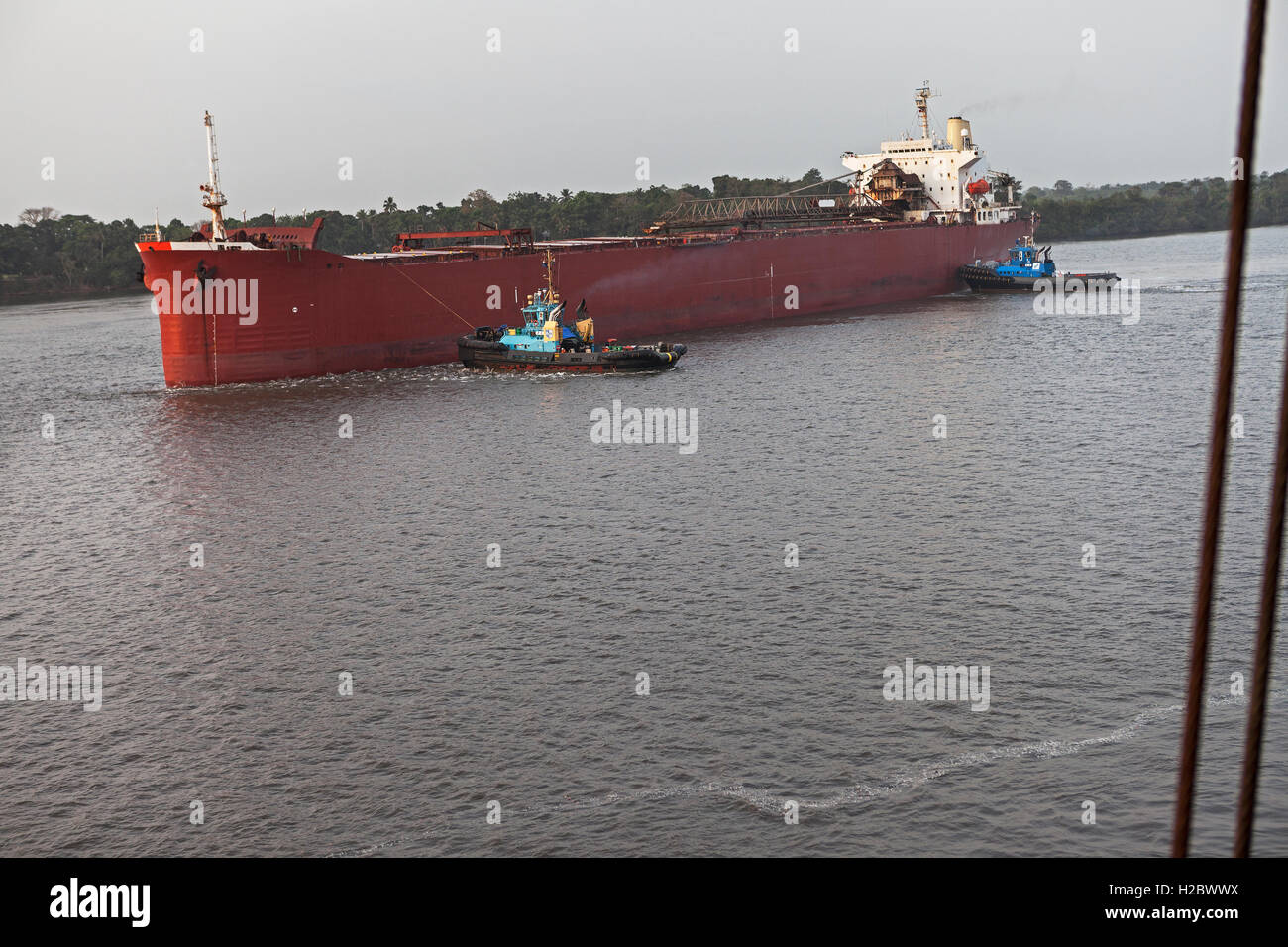 Marine und Hafen von Steg. Zwei Schlepper bewegen und drehen Frachtschiff, bevor Schiff Mauren und Anlegeplätze an der Anlegestelle und ist mit Eisenerz geladen. Stockfoto