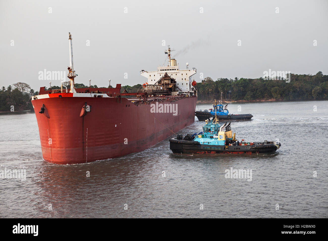 Marine und Hafen von Steg. Zwei Schlepper bewegen und drehen Frachtschiff, bevor Schiff Mauren und Anlegeplätze an der Anlegestelle und ist mit Eisenerz geladen. Stockfoto